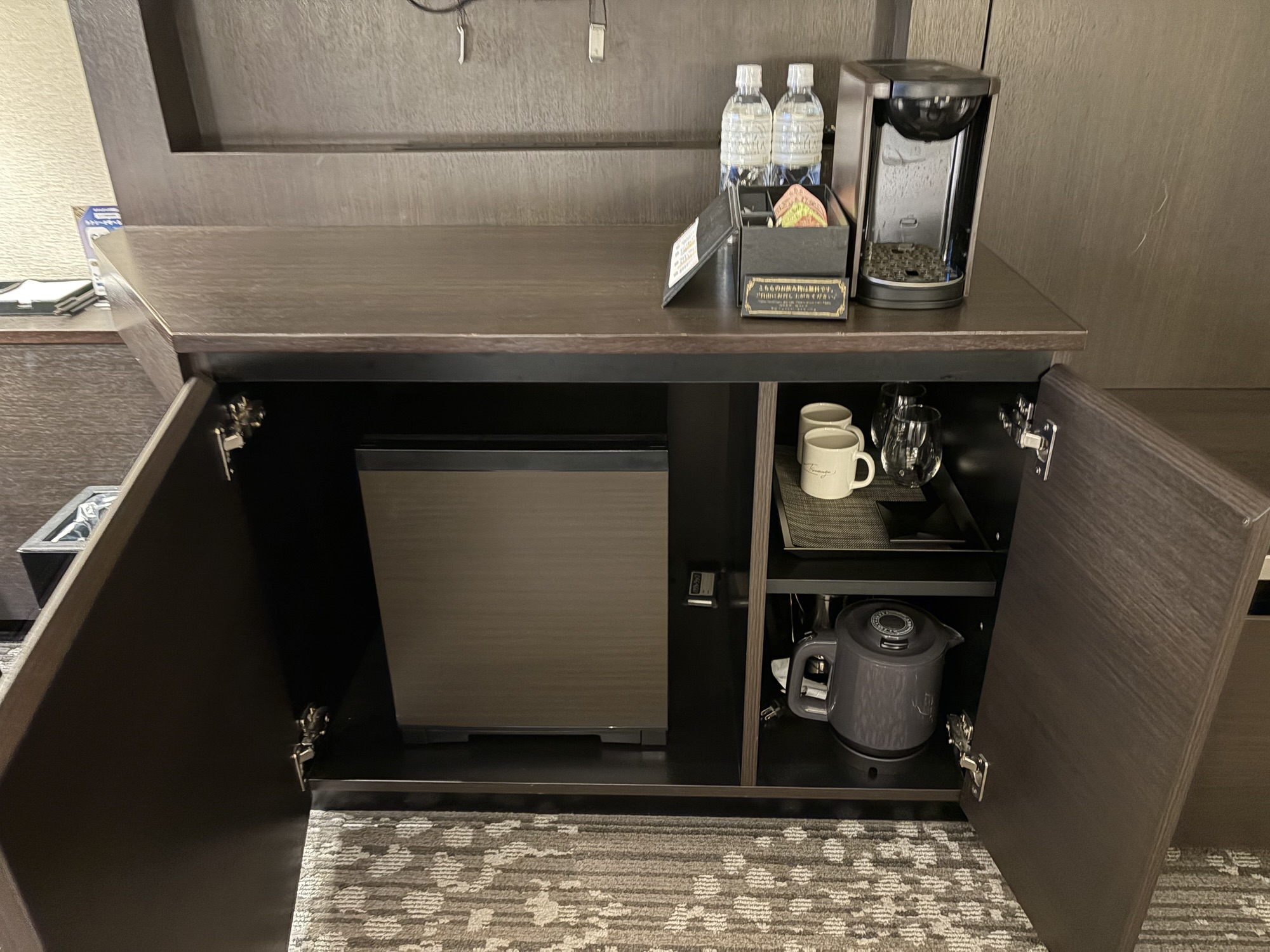 KOKO HOTEL Premier 熊本 客室のキャビネットに用意されたコンパクトな冷蔵庫、電気ケトル、無料で提供されるミネラルウォーター2本