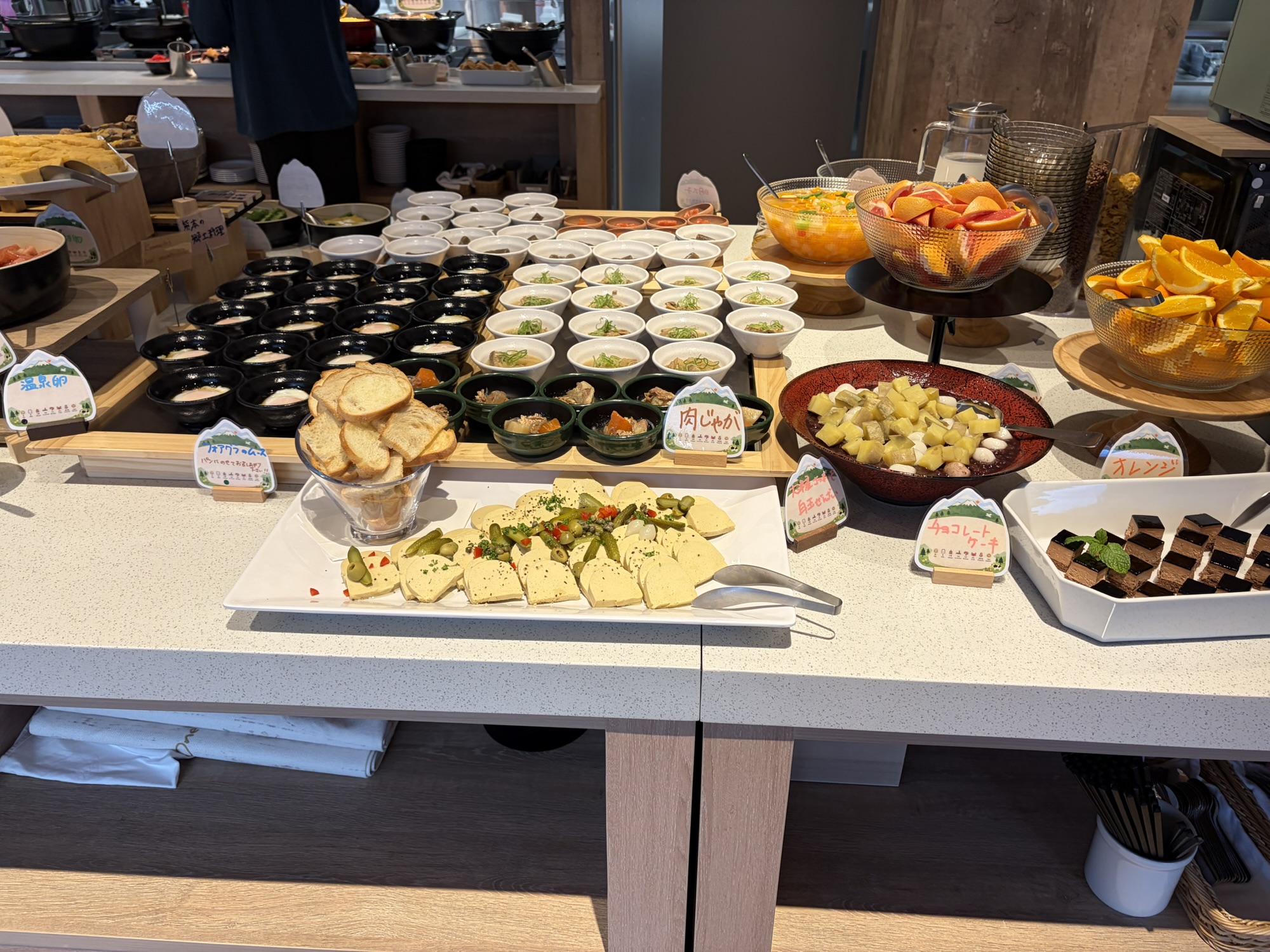 たびのホテル阿蘇熊本空港の朝食ビュッフェ。手前には珍しい「フォアグラのムース」とバゲットが置かれ、奥には温泉卵や肉じゃがなどの小鉢が豊富に並んでいます。