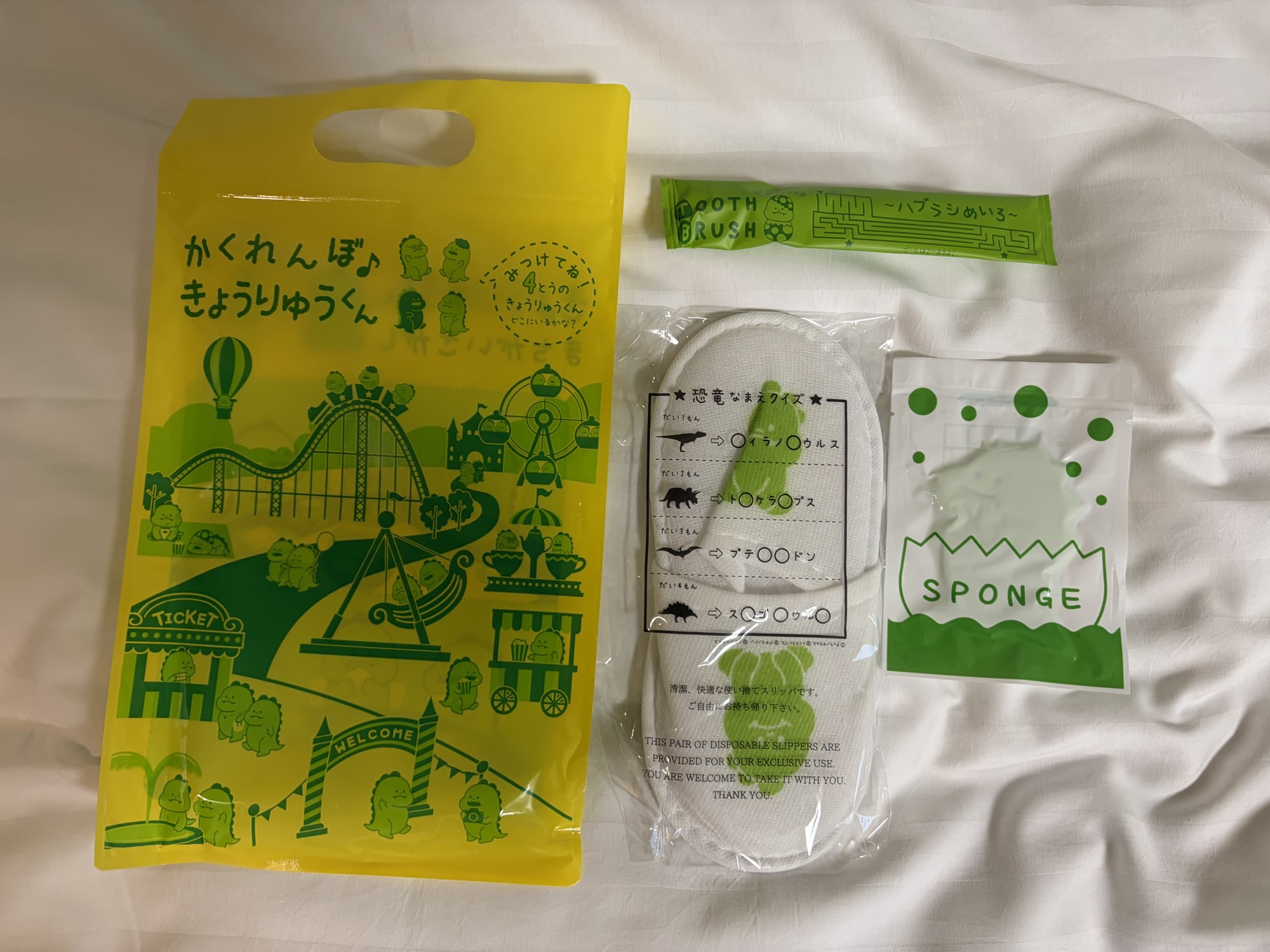 たびのホテル阿蘇熊本空港で貰える恐竜柄の子供用アメニティ。可愛い黄色い袋に、キッズサイズの歯ブラシ、スリッパ、ボディスポンジがセットになっています。