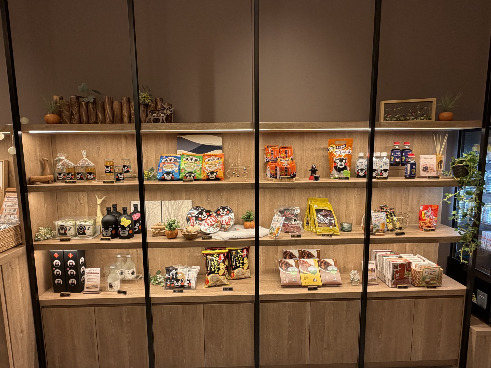 たびのホテル阿蘇熊本空港のロビーにあるお土産コーナー。くまモンパッケージのお菓子やお酒など、熊本・阿蘇の特産品が木目調の棚に並んでいます。