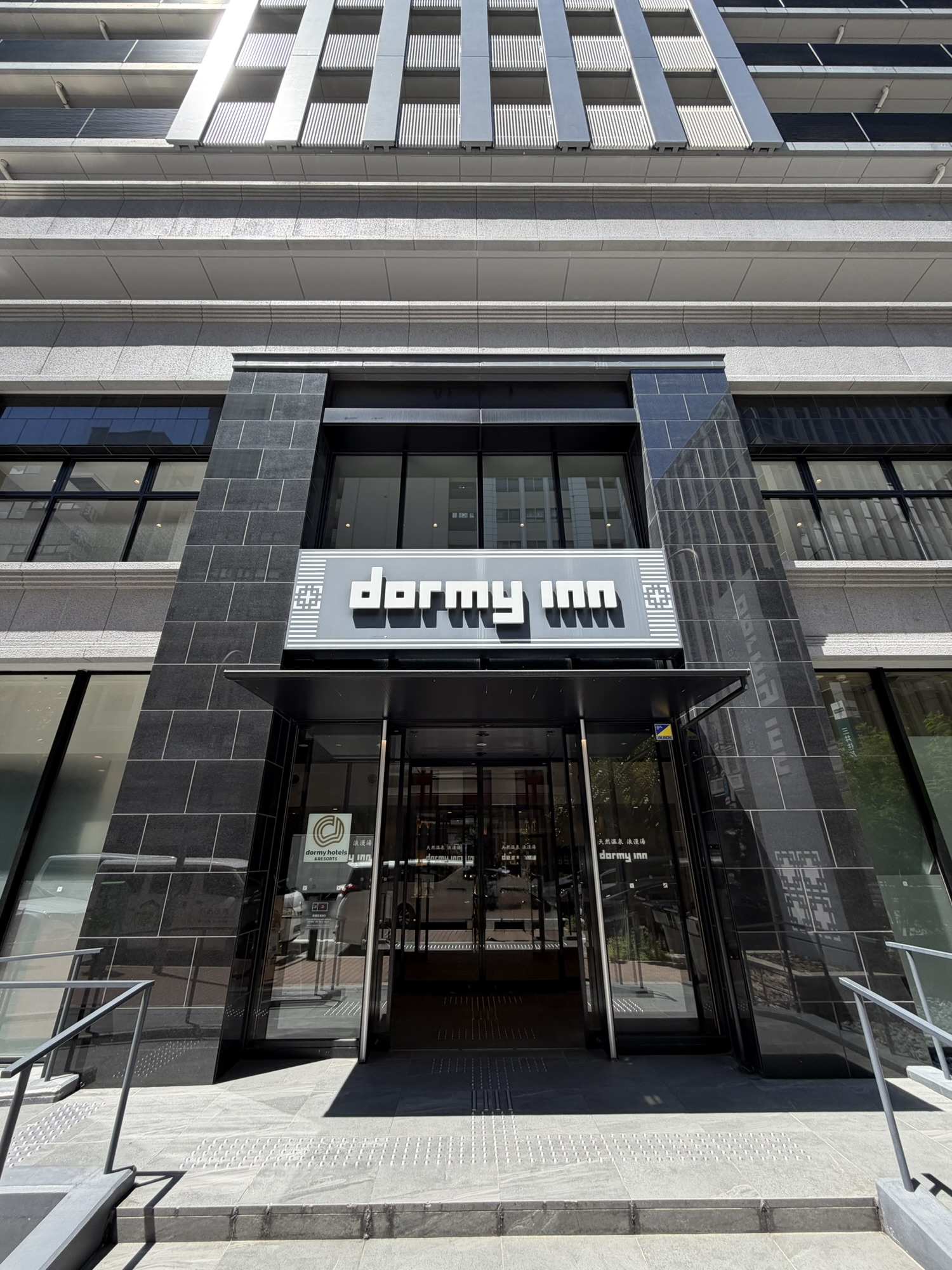 ドーミーイン神戸元町の正面エントランス。黒タイルとガラス張りのモダンな外観に「dormy inn」の看板が掲げられています。
