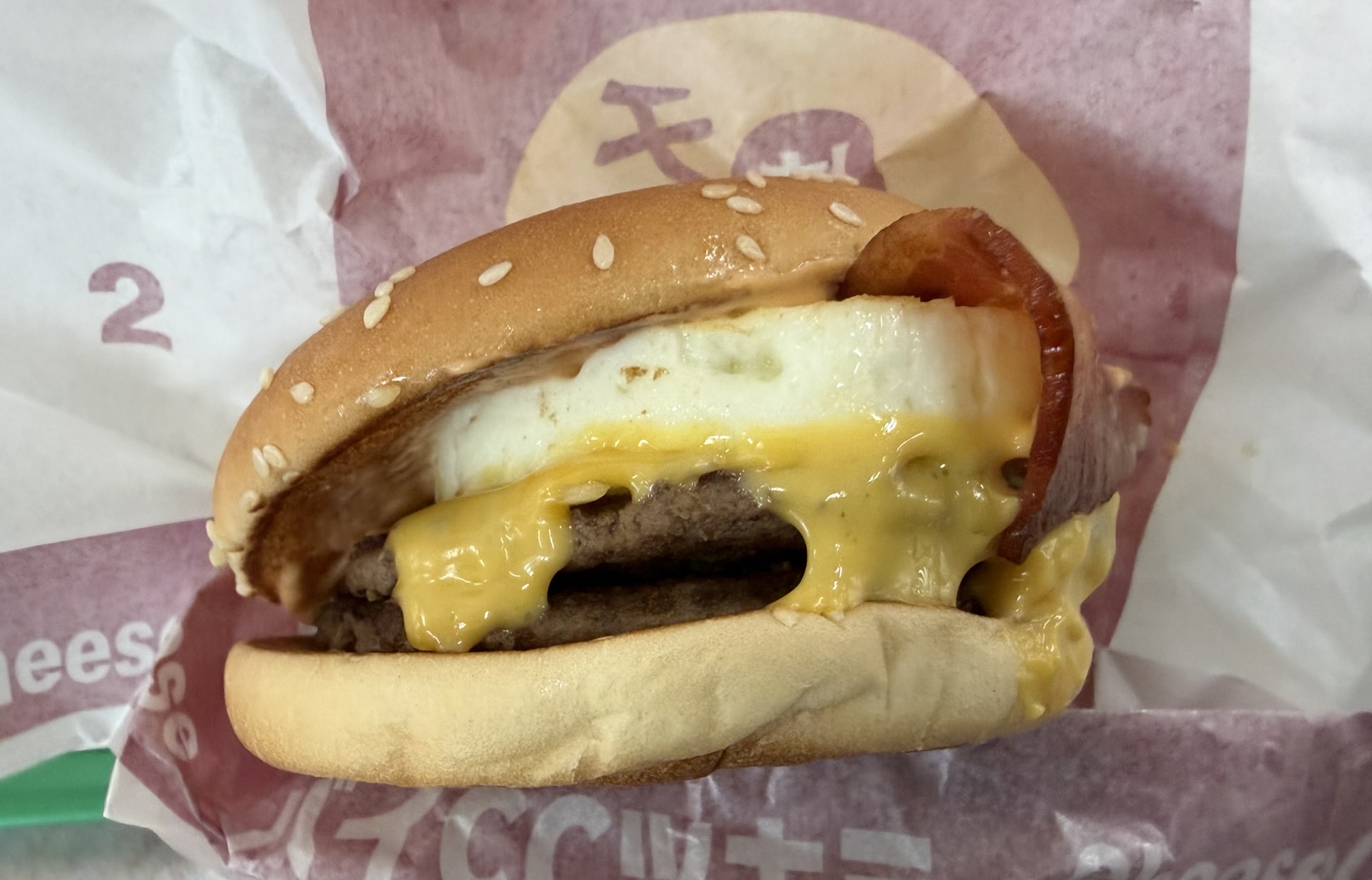 夜マック限定チーズチーズ倍月見の実物写真。ビーフパティ2枚にとろけるチェダーとホワイトチェダーの2種チーズ、目玉焼き、ベーコンがサンド